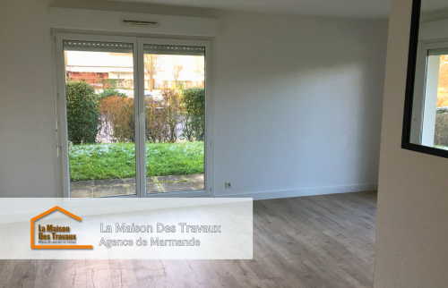 Un salon lumineux avec une grande baie vitrée donnant sur un espace extérieur verdoyant. Le parquet clair apporte une ambiance chaleureuse et moderne à la pièce, en harmonie avec les murs blancs qui accentuent la clarté de l'espace. 