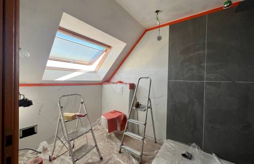 Travaux de salle de bain en cours avec carrelage effet marbre, mur foncé, WC suspendu protégé et échelles de chantier.