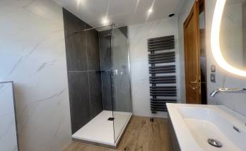 Vue finale de la salle de bain rénovée avec douche vitrée et sèche-serviettes design.