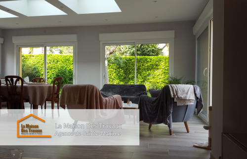 Extérieur de l'extension avec un enduit coloré chaleureux et des fenêtres en aluminium, mettant en valeur le travail minutieux des artisans.