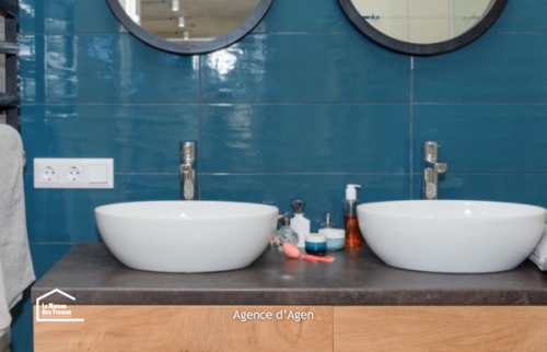 Détail d’une salle de bain rénovée à Agen : miroir rond, carrelage bleu et sèche-serviettes noir.