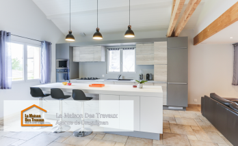 Une cuisine moderne avec un îlot central spacieux et élégant, idéal pour les repas en famille. Les suspensions noires apportent une touche de design, contrastant joliment avec les meubles en bois clair et gris.