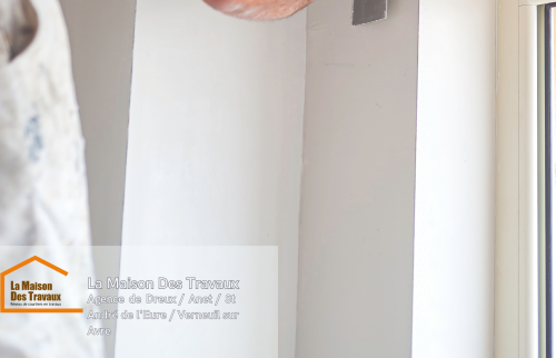 Un artisan en action, appliquant la peinture avec précision sur les encadrements de fenêtre.