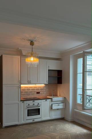 Vue d'ensemble de la cuisine ouverte, éclairée par une suspension à pampilles et un éclairage LED sous meuble.