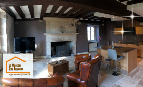 Transformation d’une pièce de vie avec cheminée et poutres apparentes, intégrant une cuisine moderne ouverte sur le salon.