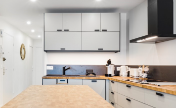 Cuisine contemporaine avec îlot central en bois massif, rangements minimalistes gris clair et hotte noire design – projet en Haute-Savoie.