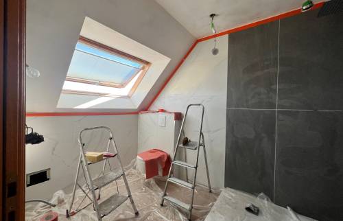 Travaux de salle de bain en cours avec carrelage effet marbre, mur foncé, WC suspendu protégé et échelles de chantier.
