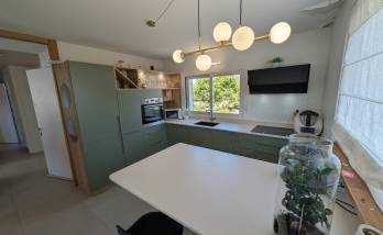 Vue d’ensemble de la cuisine contemporaine vert sauge et bois après rénovation dans une maison à Voiron.