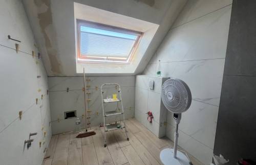 Salle de bain sous pente en cours de rénovation avec carrelage grand format effet marbre et fenêtre de toit.