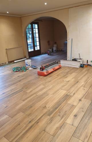 Chantier de pose du carrelage imitation bois dans le salon d’une maison à Renage.