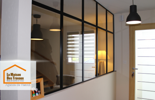 Une séparation élégante entre l’entrée et le salon grâce à une verrière d’atelier sur-mesure, apportant luminosité et style loft à cette rénovation.