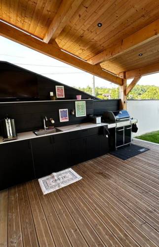 Cuisine d'été sur mesure finalisée à Coublevie avec rangements intégrés, évier, plan de travail et barbecue sous terrasse couverte.