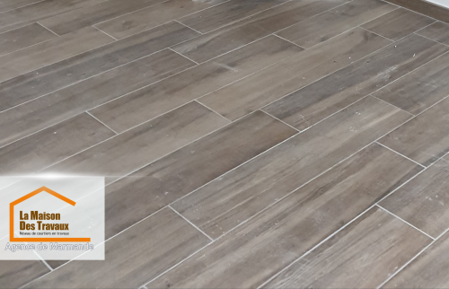 Gros plan sur le carrelage imitation bois qui donne une ambiance moderne et naturelle à la pièce. La finition impeccable reflète le travail minutieux des artisans locaux