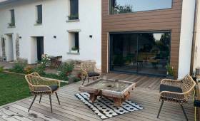 Aménagement extérieur finalisé avec terrasse bois sur-mesure devant une maison en pisé à La Côte-Saint-André : un véritable espace de vie convivial et chaleureux