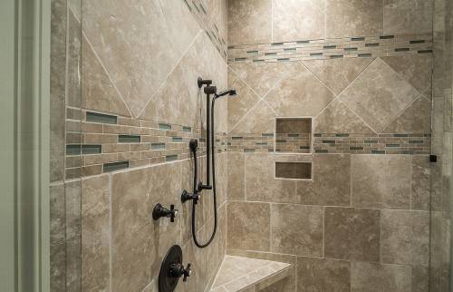 Zoom sur une douche avec carrelage en travertin posé en diagonale et frise décorative à Noyelles-Godault.