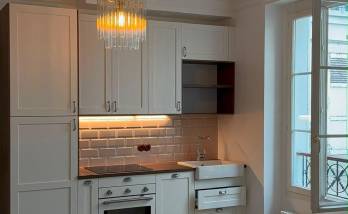 Vue d'ensemble de la cuisine ouverte, éclairée par une suspension à pampilles et un éclairage LED sous meuble.