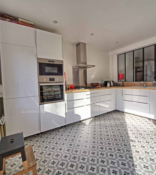 Rénovation de cuisine à Dourges style atelier : meubles blancs sans poignées, verrière noire, plan de travail en bois et sol en carreaux de ciment