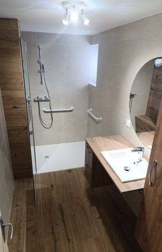 Salle de bain rénovée à Charancieu avec douche accessible, barres de maintien, meuble vasque et finitions effet bois.