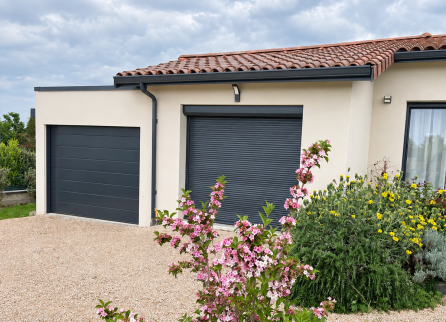 Façade du garage terminé avec enduit clair et porte anthracite, à côté de la maison.