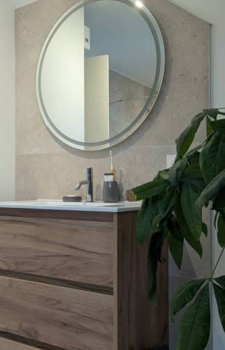 Meuble vasque en bois et miroir rond dans une salle d’eau rénovée