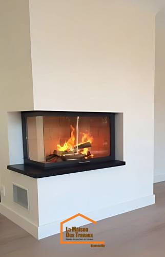 Cheminée moderne avec foyer vitré d’angle et feu de bois en fonctionnement – rénovation intérieure à Bonneville en Haute-Savoie.