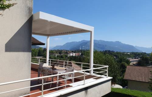 Vue extérieure de la pergola bioclimatique blanche, intégrée à la façade et aux garde-corps de la résidence.