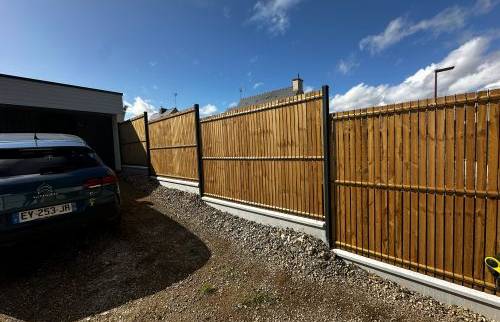 Mise en place d’une clôture rigide en bois sur muret existant, permettant de sécuriser le terrain tout en préservant l’esthétique extérieure.