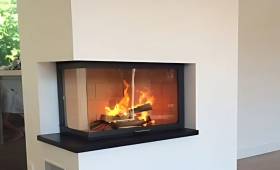 Cheminée moderne avec foyer vitré d’angle et feu de bois en fonctionnement – rénovation intérieure à Bonneville en Haute-Savoie.