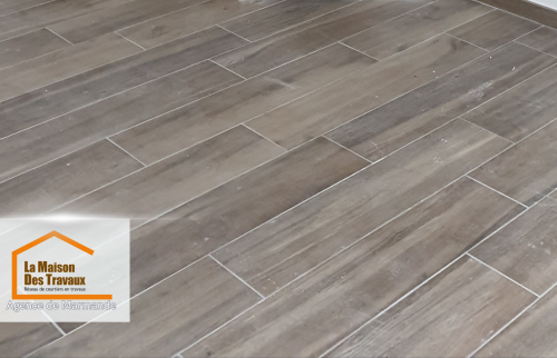 Gros plan sur le carrelage imitation bois qui donne une ambiance moderne et naturelle à la pièce. La finition impeccable reflète le travail minutieux des artisans locaux