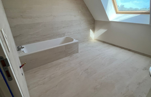 Vue d’ensemble de la salle de bain après rénovation avec baignoire et travertin