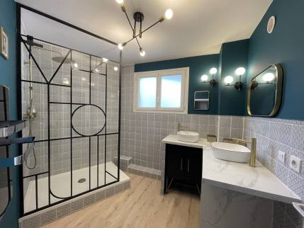 Vue d’ensemble d’une salle de bain rénovée à Carqueiranne, avec douche à l’italienne, verrière noire style atelier et éclairage moderne au plafond.