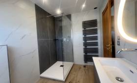 Vue finale de la salle de bain rénovée avec douche vitrée et sèche-serviettes design.
