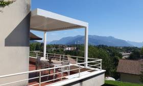 Vue extérieure de la pergola bioclimatique blanche, intégrée à la façade et aux garde-corps de la résidence.