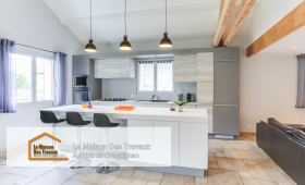 Une cuisine moderne avec un îlot central spacieux et élégant, idéal pour les repas en famille. Les suspensions noires apportent une touche de design, contrastant joliment avec les meubles en bois clair et gris.