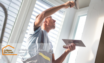 Un artisan en plein travail sur un mur, appliquant un enduit avec précision pour lisser les imperfections. 