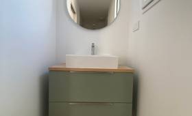 Meuble vasque suspendu vert sauge avec plan effet bois et miroir rond dans une salle d'eau à Damgan