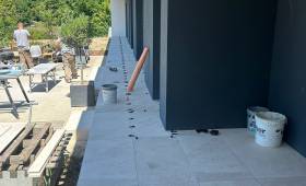 Pose d’un carrelage extérieur grand format pour la création d’une terrasse contemporaine autour d’une maison à Voiron.