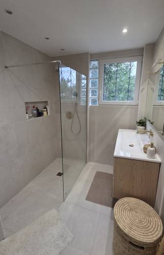 Douche à l’italienne avec paroi vitrée transparente, carrelage beige, niche murale de rangement et robinetterie dorée.