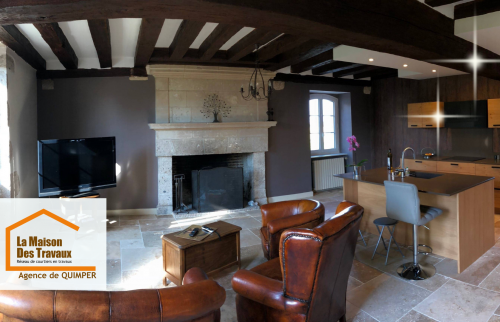 Transformation d’une pièce de vie avec cheminée et poutres apparentes, intégrant une cuisine moderne ouverte sur le salon.