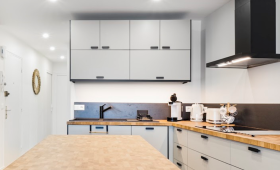 Cuisine contemporaine avec îlot central en bois massif, rangements minimalistes gris clair et hotte noire design – projet en Haute-Savoie.