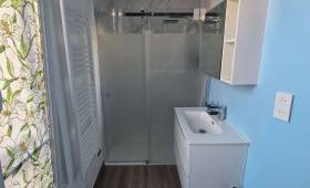 Salle de bains moderne rénovée avec meuble vasque blanc, miroir rond et douche vitrée