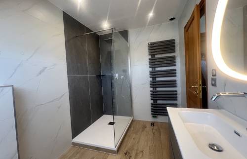Vue finale de la salle de bain rénovée avec douche vitrée et sèche-serviettes design.