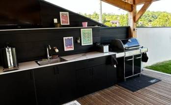 Cuisine d'été sur mesure finalisée à Coublevie avec rangements intégrés, évier, plan de travail et barbecue sous terrasse couverte.