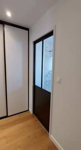 Porte coulissante de type verrière d'atelier intégrée à la cloison pour accéder à la salle de bain depuis le dressing