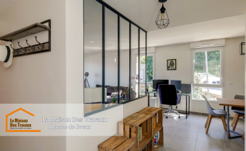 Une verrière élégante sépare l’entrée du salon, apportant une touche industrielle moderne et laissant entrer la lumière naturelle.