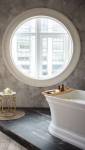 Une salle de bain avec une fenêtre ronde une baignoire et des murs couverts de tadelakt gris 