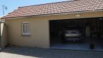Réalisation d'un garage double avec portail coulissant, attenant à une maison existante, commune de l'ouest de Lyon : cour gravillonnée et porte sectionnelle motorisée