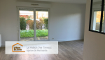 Un salon lumineux avec une grande baie vitrée donnant sur un espace extérieur verdoyant. Le parquet clair apporte une ambiance chaleureuse et moderne à la pièce, en harmonie avec les murs blancs qui accentuent la clarté de l'espace. 
