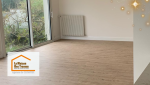 Le salon baigné de lumière naturelle grâce à de larges baies vitrées, sublimé par un parquet clair qui agrandit l’espace.