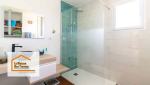 Gros plan sur la douche à l’italienne, avec des carreaux vert émeraude au design contemporain, un mitigeur et une douche de tête élégants. Une paroi vitrée épurée sépare harmonieusement la zone de douche du reste de la pièce.